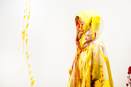side view of woman in raincoat painted with yellow and red paints standing in hood isolated on whiteの写真素材