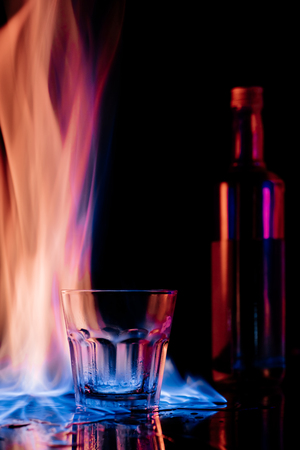 close up view of flame, empty glass and bottle of sambuca alcohol drink on black backgroundの写真素材