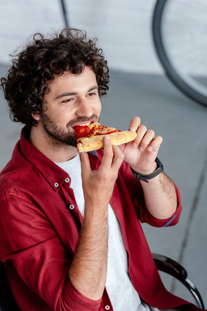 high angle view of young man eating pizza and looking awayの写真素材
