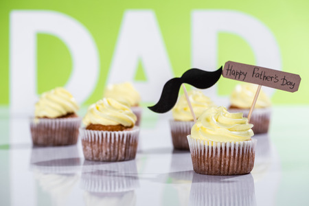 creamy cupcakes with mustache sign and Happy fathers day inscription in front of dad inscription made of white letters on greenの写真素材