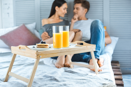 selective focus of multicultural couple and breakfast on wooden tray on bed in bedroomの写真素材