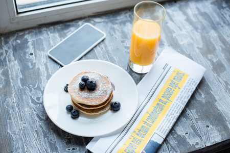 close up view of pancakes, glass of juice, smartphone and newspaper on wooden tabletopの写真素材