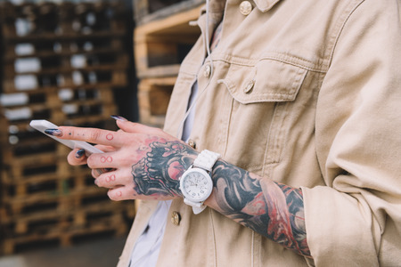 cropped image of tattooed woman with wristwatch using smartphone