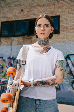 young attractive tattooed girl holding skateboard at streetの写真素材