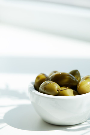 closeup shot of bowl with green olives on white tableの写真素材