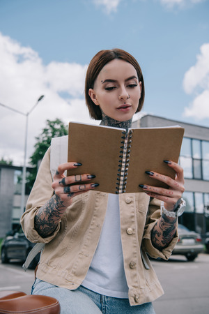 low angle view of stylish tattooed woman reading textbook at streetの写真素材