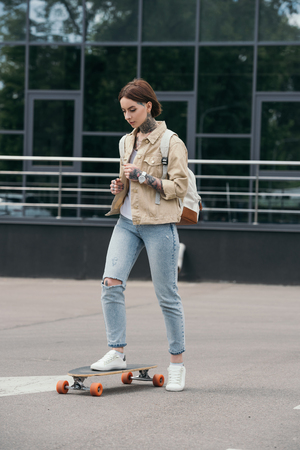 young stylish tattooed woman skateboarding at streetの写真素材