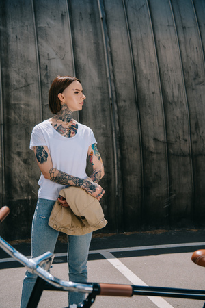 side view of stylish woman with tattoos looking away near bicycleの写真素材