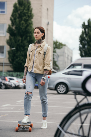selective focus of stylish tattooed woman skateboarding at parking lotの写真素材