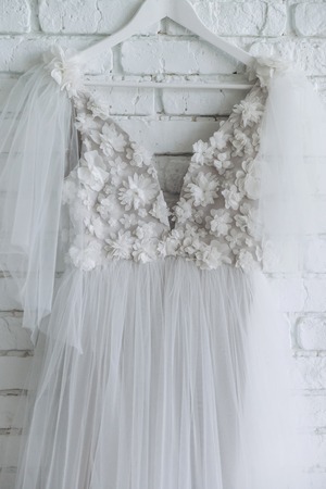 stylish wedding dress decorated with flowers hanging on white brick wallの写真素材