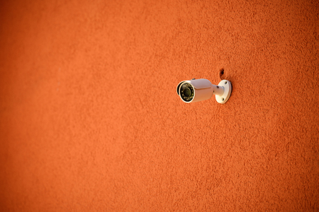 close up view of security camera on orange colored building facade