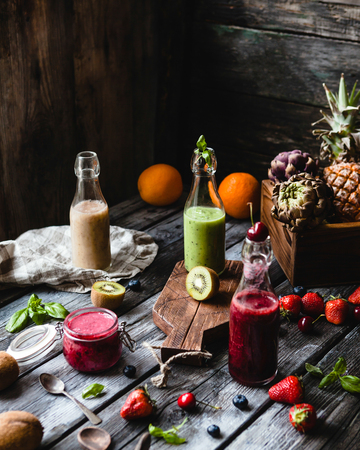 Fresh healthy smoothies in glass bottles on rustic table with assorted fruitsの写真素材