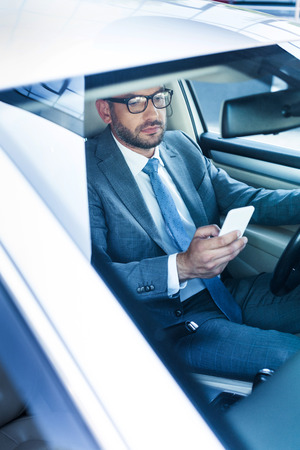 portrait of businessman with smartphone driving carの写真素材