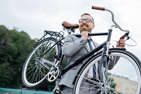 smiling bearded businessman in grey suit holding bikeの写真素材