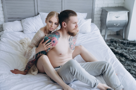 attractive young woman embracing her boyfriend from behind while sitting in bedの写真素材