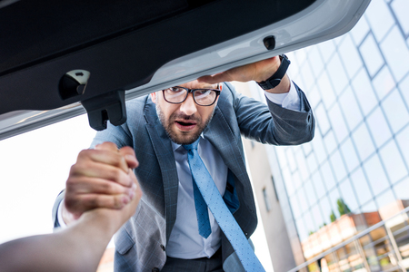 partial view of businessman holding hand of man in luggage boot of carの写真素材