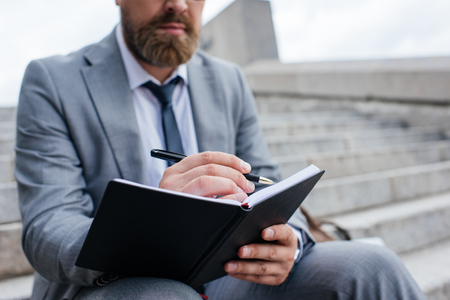 cropped view of businessman writing in diary and sitting on stairsの写真素材