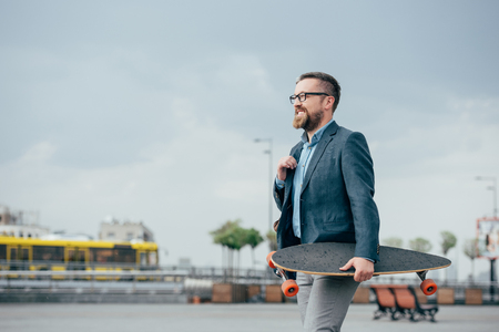 stylish bearded man with skate walking in cityの写真素材