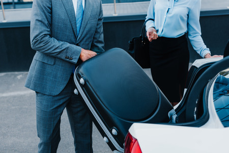 cropped shot of businessman putting baggage into car with colleague near byの写真素材
