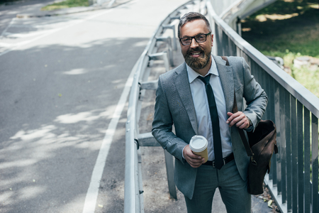businessman in suit with leather bag and coffee to go walking in cityの写真素材