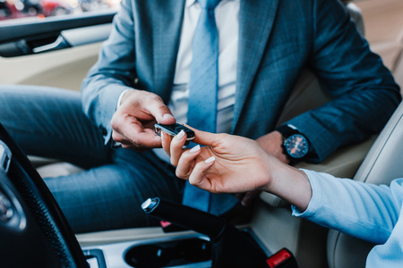 cropped shot of businessman giving car keys to colleague at driver seat in carの写真素材