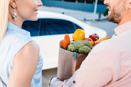 cropped shot of married couple with paper bag full of healthy food on parking near carの写真素材