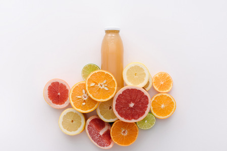 top view of bottle of juice with citrus fruits slices on white surfaceの写真素材