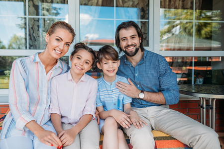 portrait of smiling family sitting on sofa together on country house porchの写真素材