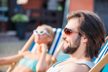 selective focus of smiling man spending time near swimming pool together with wife on backyard on summer dayの写真素材