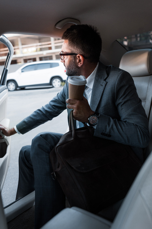 businessman with coffee to go sitting in car with opened doorの写真素材