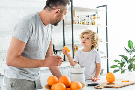 son and father looking at each other after making fresh orange juice at kithenの写真素材