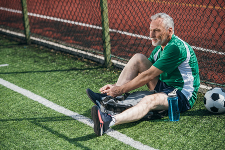 side view of old man tying shoelaces on football fieldの写真素材