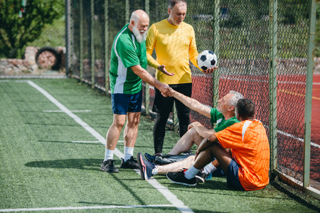 interracial elderly football players shaking hands after match on green fieldの写真素材