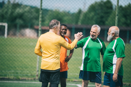 interracial elderly football players shaking hands after match on green fieldの写真素材