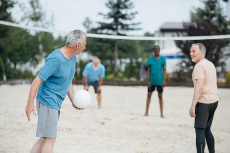 selective focus of multicultural old friends playing volleyball on beach on summer dayの写真素材