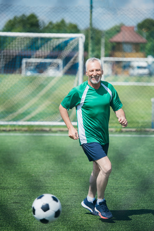 cheerful old man playing football on field on summer dayの写真素材