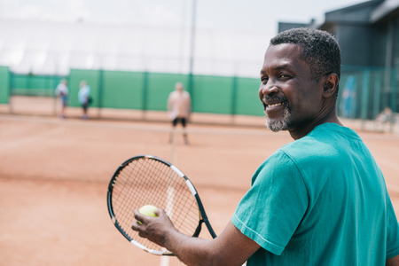 selective focus of smiling elderly african american man playing tennis with friend on courtの写真素材