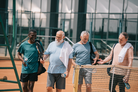portrait of smiling multiracial elderly friends with tennis equipment on courtの写真素材