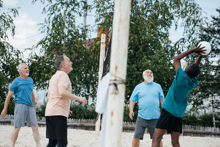 side view of multicultural old friends playing volleyball on beach on summer dayの写真素材