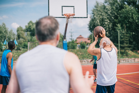 selective focus of interracial elderly sportsmen playing basketball together on playgroundの写真素材