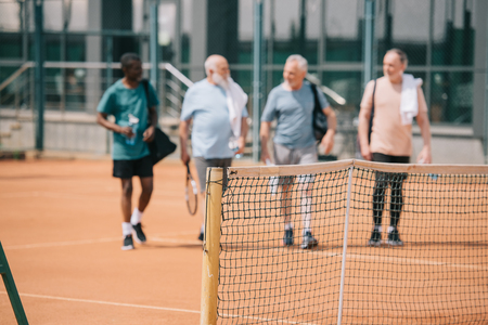 selective focus of multiracial elderly friends with tennis equipment on courtの写真素材