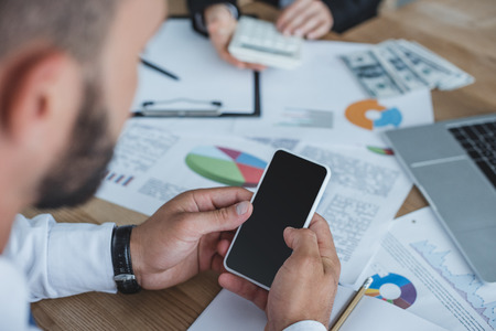 cropped image of financier using smartphone at table in officeの写真素材