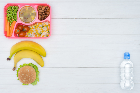 top view of tray with kids lunch for school, bananas and plastic bottle of water on white tableの写真素材
