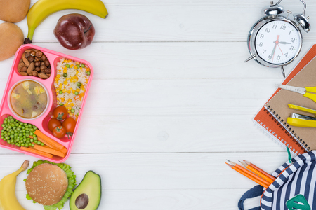 top view of kids lunch for school and alarm clock with bag on wooden tableの写真素材
