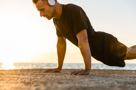 athletic adult man in headphones doing push ups on seashoreの写真素材