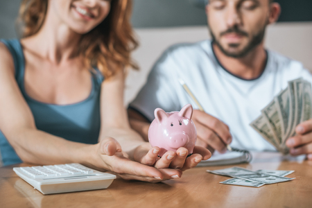 cropped image of couple planning family budget and holding piggy bank in living roomの写真素材