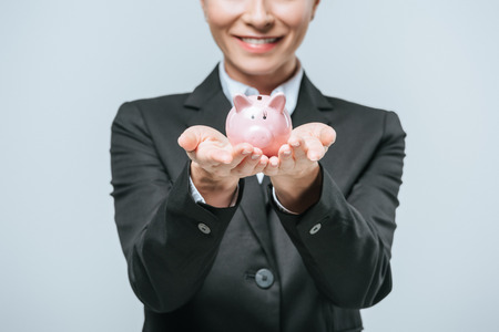 cropped image of smiling financier holding piggy bank isolated on greyの写真素材
