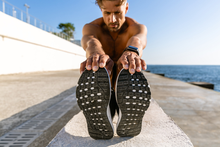 close-up shot of adult shirtless sportsman stretching before training on seashoreの写真素材