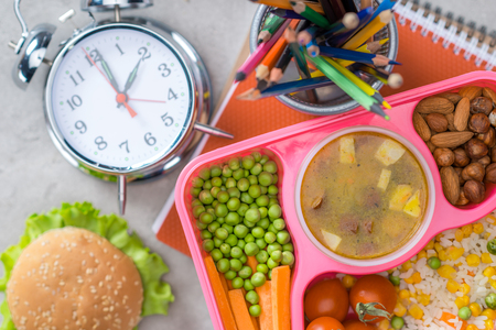 top view of tray with kids lunch for school, alarm clock and colored pencils on tableの写真素材