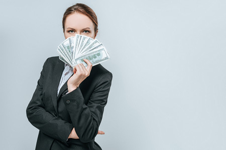beautiful financier looking out from pack of dollar banknotes isolated on greyの写真素材